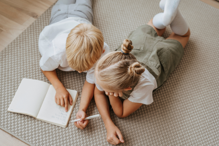 Dwoje dzieci, rodzeństwo, brat i siostra leżą na dywanie i wspólnie spędzają czas czytając książkę.